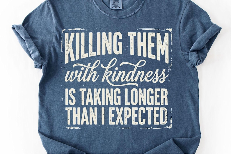K&ouml;nnte beinhalten: Ein marineblaues T-Shirt mit dem wei&szlig;en Aufdruck &bdquo;KILLING THEM with kindness IS TAKING LONGER THAN I EXPECTED&ldquo; im Used-Look. Das Shirt hat hochgekrempelte &Auml;rmel und einen Rundhalsausschnitt.
