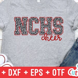Puede incluir: Una camiseta gris con un contorno rojo de las letras "NCHS" en estampado de leopardo blanco y negro. La palabra "cheer" est&aacute; escrita en cursiva roja debajo de las letras.