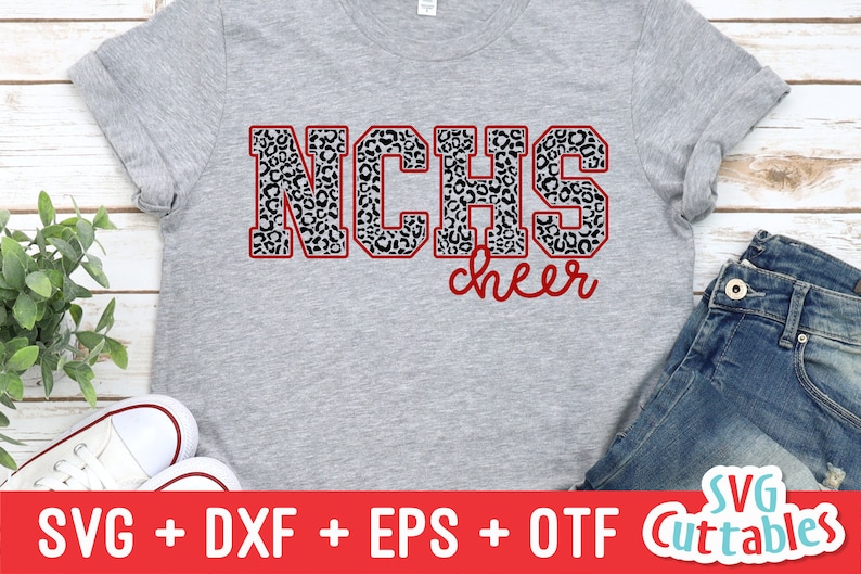 Puede incluir: Una camiseta gris con un contorno rojo de las letras "NCHS" en estampado de leopardo blanco y negro. La palabra "cheer" est&aacute; escrita en cursiva roja debajo de las letras.