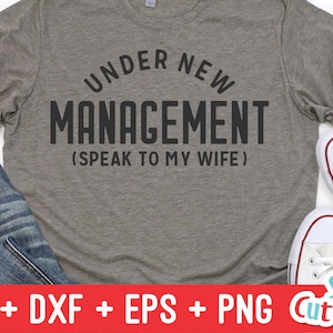 May include: A gray t-shirt with the text "Under New Management (Speak to My Wife)" printed in black.
