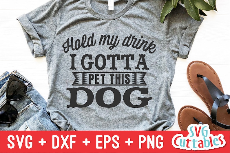 May include: A gray t-shirt with the text "Hold my drink I GOTTA PET THIS DOG" printed in black. The text is in a bold, blocky font. The shirt is a popular design for dog lovers.
