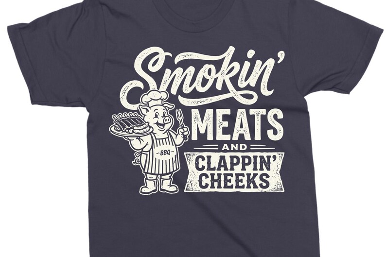 May include: Dark navy blue t-shirt with a white graphic. The graphic features the text "Smokin' Meats and Clappin' Cheeks" in a vintage style. A cartoon pig wearing a chef's hat and apron is holding a plate of ribs.