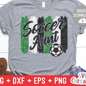 May include: A gray t-shirt with a green, white, and black glitter design that says "Soccer Aunt" with a soccer ball in the center.