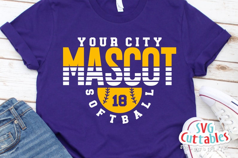 以下が含まれることがあります： 紫色のTシャツに「YOUR CITY MASCOT SOFTBALL」という文字が白と黄色で書かれています。「MASCOT」という文字は、黄色い背景に大きく太字で書かれています。「SOFTBALL」という文字は、黄色のソフトボールと「18」という数字が書かれた円の中にあります。