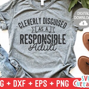 May include: A gray t-shirt with the text "CLEVERLY DISGUISED AS A RESPONSIBLE Adult" in black. The shirt is on a blue denim background with a pair of sunglasses and brown sandals.