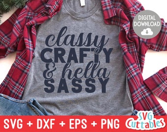 May include: A gray t-shirt with the text "classy CRAFTY & hella SASSY" in dark blue lettering. The shirt is laying on a red and black plaid flannel shirt.