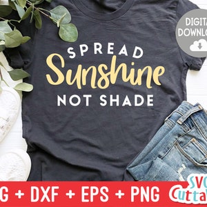 May include: A black t-shirt with the text "SPREAD Sunshine NOT SHADE" in white and yellow lettering. The shirt is laying on a white surface with a pair of white shoes and blue jeans.