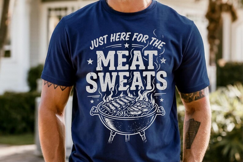 May include: Navy blue t-shirt with the text "JUST HERE FOR THE MEAT SWEATS" in white. A graphic of a grill with ribs and steak is below the text. The shirt is a casual wear item.
