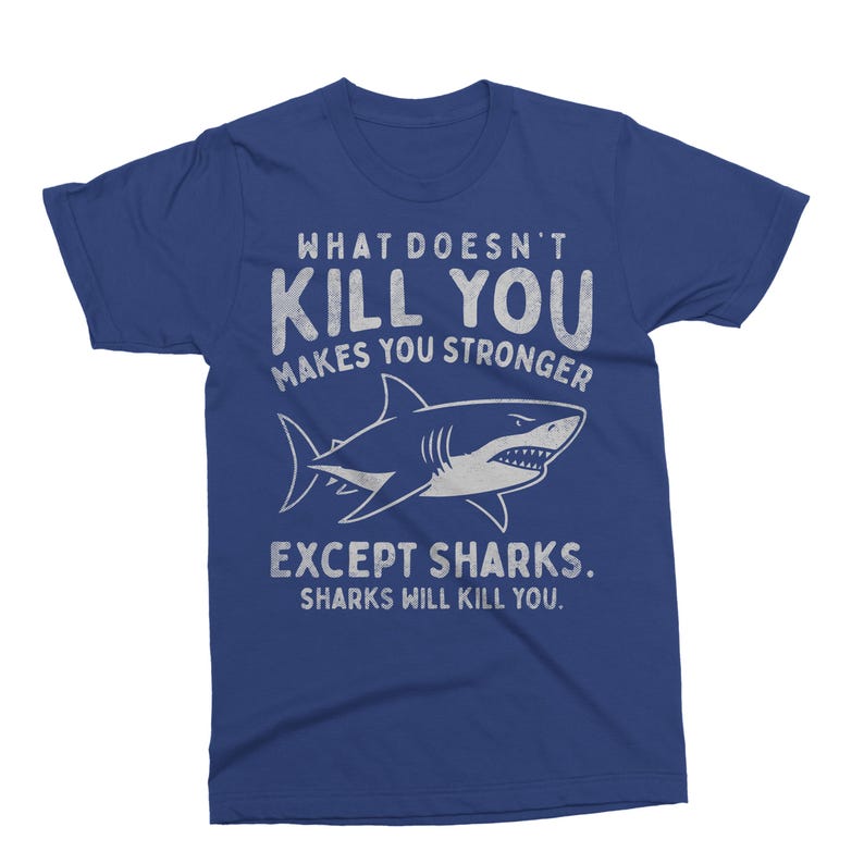 May include: A blue t-shirt with the text "WHAT DOESN'T KILL YOU MAKES YOU STRONGER EXCEPT SHARKS. SHARKS WILL KILL YOU." A white shark illustration is featured below the text. The shirt is a crew neck style.