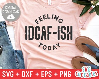 May include: A pink t-shirt with the text "Feeling IDGAF-ISH Today" in black lettering. The shirt is on a white surface with a pair of brown sandals and a pair of jeans.