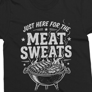 May include: Black t-shirt with a white graphic. The graphic features the text "JUST HERE FOR THE MEAT SWEATS" above an illustration of a barbecue grill with ribs and a steak. Stars and flames are also included in the design.