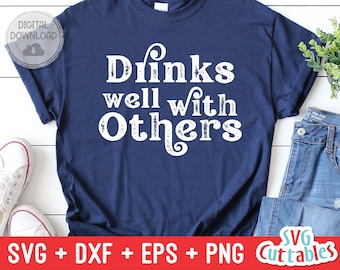May include: A navy blue t-shirt with white text that reads "Drinks well with others". The text has a distressed look. The shirt is on a white surface with a pair of white sneakers and a pair of blue jeans.