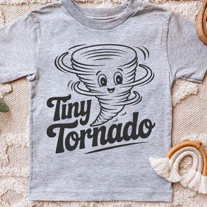 Peut inclure: T-shirt gris clair avec un dessin de tornade de dessin anim&eacute; souriante. Le texte "Tiny Tornado" est imprim&eacute; en noir en dessous. Le t-shirt est fabriqu&eacute; dans une mati&egrave;re douce.