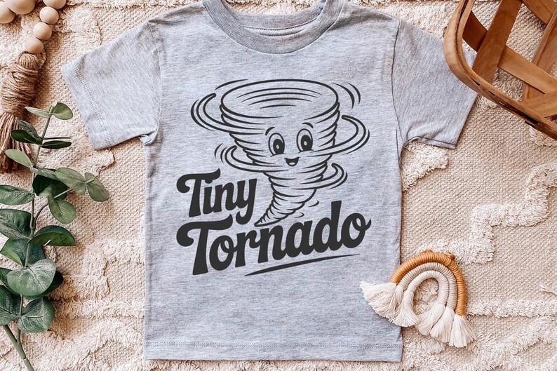 Peut inclure: T-shirt gris clair avec un dessin de tornade de dessin anim&eacute; souriante. Le texte "Tiny Tornado" est imprim&eacute; en noir en dessous. Le t-shirt est fabriqu&eacute; dans une mati&egrave;re douce.