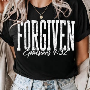 May include: Black t-shirt with the word "FORGIVEN" in large, distressed white letters. Below, in a smaller, cursive font, is "Ephesians 4:32". The shirt is a classic crew neck style.