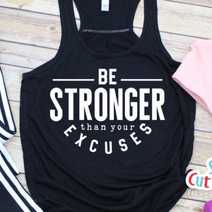 May include: Black tank top with white text that reads "BE STRONGER than your EXCUSES". The tank top is laying on a wooden surface with a pair of black leggings with white stripes, a pink tank top, and pink weights.