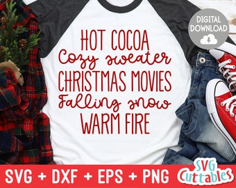 May include: A white long-sleeved shirt with a red graphic design that reads "HOT COCOA Cozy sweater CHRISTMAS MOVIES Falling snow WARM FIRE". The shirt is on a red and black plaid surface.