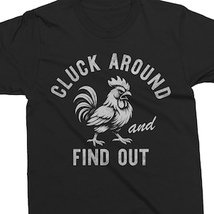 Puede incluir: Camiseta negra con un diseño gráfico blanco desgastado de un gallo y el texto "CLUCK AROUND and FIND OUT". El diseño presenta una ilustración detallada de un gallo con el texto en una fuente audaz y vintage.