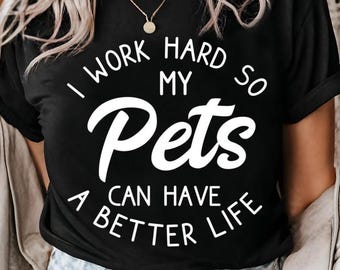 May include: Black t-shirt with the white text "I WORK HARD SO MY Pets CAN HAVE A BETTER LIFE." The shirt has a crew neck and short sleeves. A gold necklace is visible.