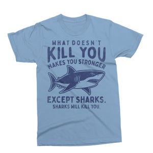 May include: Light blue t-shirt with the text "WHAT DOESN'T KILL YOU MAKES YOU STRONGER EXCEPT SHARKS. SHARKS WILL KILL YOU." and a navy blue shark graphic.