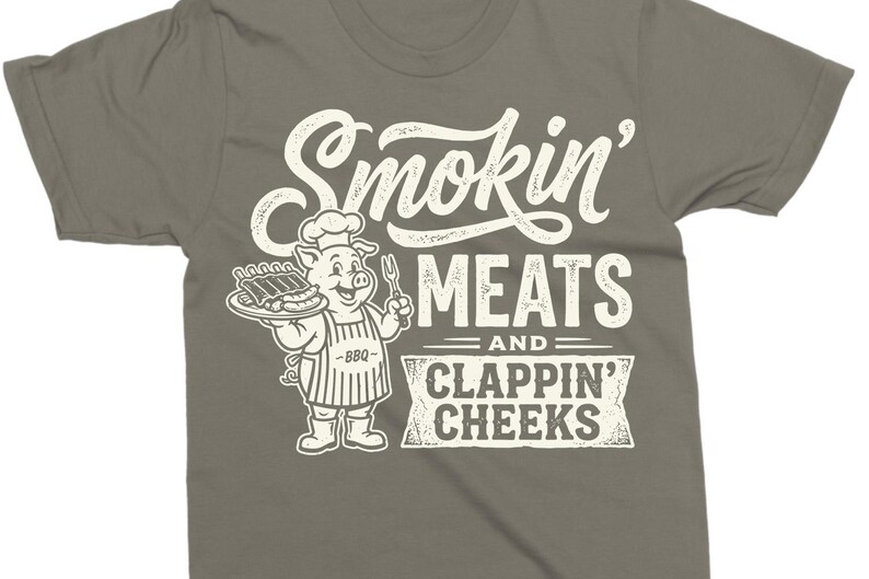 May include: Gray t-shirt with a graphic featuring a cartoon pig chef holding a plate of ribs and a fork. The text reads "Smokin' MEATS and CLAPPIN' CHEEKS" in a vintage style.