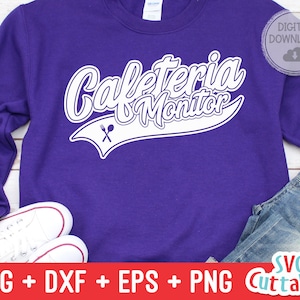 May include: A purple sweatshirt with the text "Cafeteria Monitor" in white with a fork and spoon graphic. The text is in a white baseball-style font.