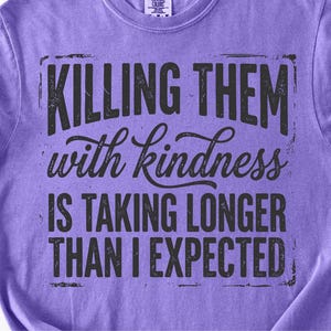 K&ouml;nnte beinhalten: Ein lilafarbenes T-Shirt mit dem schwarzen Text: "KILLING THEM with kindness IS TAKING LONGER THAN I EXPECTED". Der Text hat einen Used-Look. Das T-Shirt hat einen Rundhalsausschnitt und kurze &Auml;rmel.