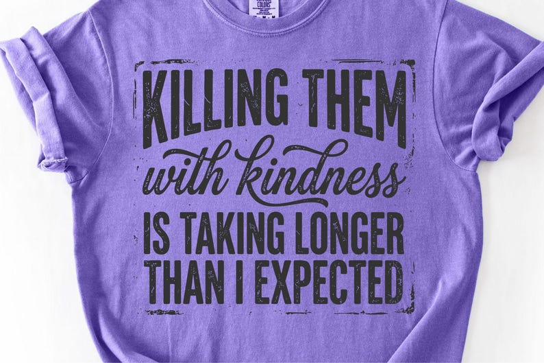 K&ouml;nnte beinhalten: Ein lilafarbenes T-Shirt mit dem schwarzen Text: "KILLING THEM with kindness IS TAKING LONGER THAN I EXPECTED". Der Text hat einen Used-Look. Das T-Shirt hat einen Rundhalsausschnitt und kurze &Auml;rmel.