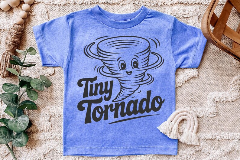 Peut inclure: T-shirt bleu clair avec un dessin anim&eacute; de tornade souriante et l'inscription "Tiny Tornado" en noir. Le t-shirt est en tissu doux.