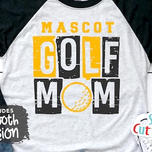Pu&ograve; includere: Una maglietta da baseball bianca e nera con una grafica gialla e nera distressed che dice "Mascot Golf Mom" con una palla da golf al centro. La maglietta ha maniche nere e un corpo bianco.
