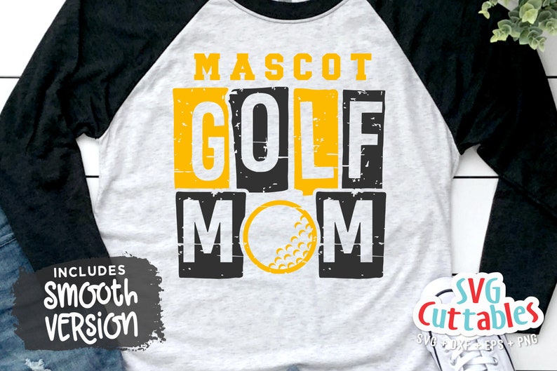 Pu&ograve; includere: Una maglietta da baseball bianca e nera con una grafica gialla e nera distressed che dice "Mascot Golf Mom" con una palla da golf al centro. La maglietta ha maniche nere e un corpo bianco.