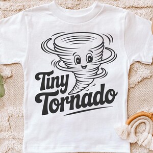 Peut inclure: T-shirt blanc avec un dessin anim&eacute; en noir et blanc d'une tornade souriante. Le texte "Tiny Tornado" est &eacute;crit en dessous dans une police de caract&egrave;res audacieuse et amusante. Un design amusant pour les enfants.