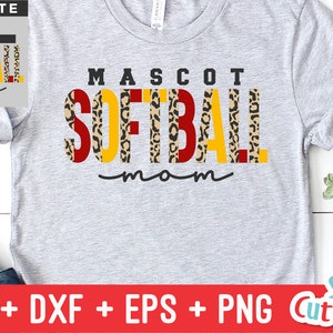 Pu&ograve; includere: Una maglietta grigia con il testo "MASCOT SOFTBALL mom" in lettere nere, rosse e gialle con uno schema a stampa leopardata. Il testo &egrave; in grassetto, in un carattere a blocchi.