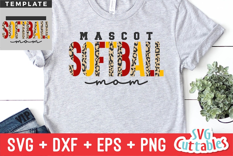 Pu&ograve; includere: Una maglietta grigia con il testo "MASCOT SOFTBALL mom" in lettere nere, rosse e gialle con uno schema a stampa leopardata. Il testo &egrave; in grassetto, in un carattere a blocchi.