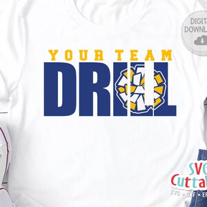 May include: White t-shirt with the text "Your Team Drill" in blue and yellow letters. A cheerleading pom pom is in the middle of the text. The text "SVG Cuttables" is in the bottom right corner of the image.