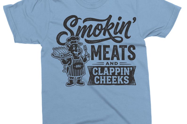 May include: Light blue t-shirt with the text "Smokin' MEATS and CLAPPIN' CHEEKS". The shirt features a cartoon pig chef holding a platter of ribs and a fork. The design is in black.