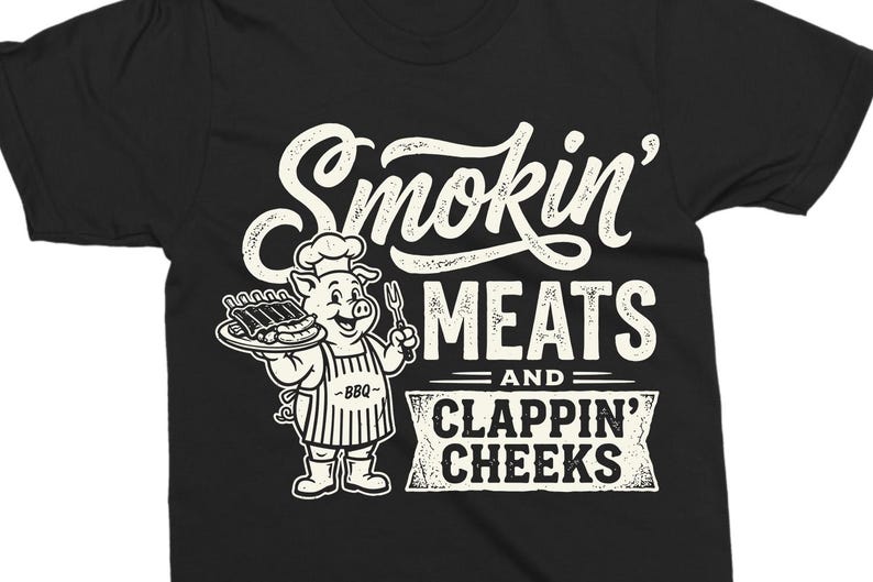 May include: Black t-shirt with a white graphic. The graphic features a cartoon pig chef holding a plate of ribs and a fork, with the words "Smokin' MEATS and CLAPPIN' CHEEKS" in a vintage style.