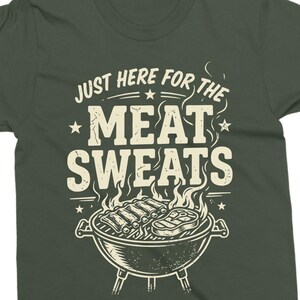 May include: Dark green t-shirt with the text "JUST HERE FOR THE MEAT SWEATS" in a distressed font. Below the text is a graphic of a barbecue grill with ribs and a steak, with flames rising.