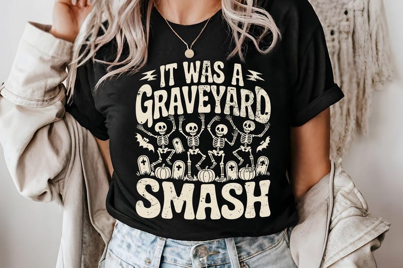 May include: Black t-shirt with the text "IT WAS A GRAVEYARD SMASH" in a distressed font. The graphic features dancing skeletons, pumpkins, and tombstones, perfect for Halloween.