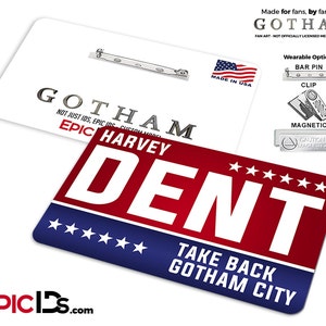 May include: A red, white, and blue badge with the text "GOTHAM" and "DENT" in white. The badge also includes the text "HARVEY" and "TAKE BACK GOTHAM CITY". The badge is made in the USA and has multiple wearable options: bar pin, clip, and magnetic.