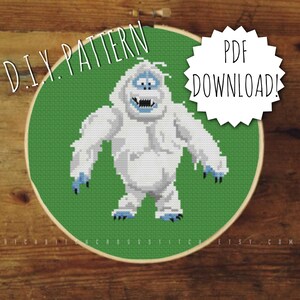 May include: A cross-stitch pattern of a white yeti with blue details, displayed on a green backdrop within an embroidery hoop. Text includes "D.I.Y. PATTERN" and "PDF DOWNLOAD!", suitable for crafting projects.