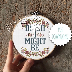 以下が含まれることがあります： 白い刺繍枠に、「B*tch I might be」と刺繍されたクロスステッチパターンが、花の縁取りで囲まれています。枠は手で持たれています。右上に「PDF DOWNLOAD!」と書かれた星形のステッカーがあります。