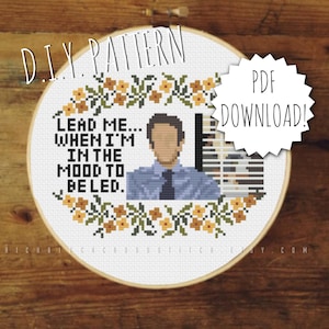 May include: A round embroidery hoop with white fabric inside. The fabric has a cross-stitch pattern of a man with brown hair, wearing a blue shirt and a tie. The text "LEAD ME... WHEN I'M IN THE MOOD TO BE LED." is stitched in black thread around the man's image. The hoop is surrounded by a wooden frame. A white sticker with black text that says "PDF DOWNLOAD!" is on the right side of the hoop.