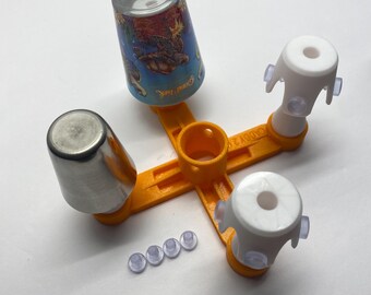 May include: An orange plastic caddy with the text CADDY 2.0, featuring three white cylindrical attachments with small clear suction cups. One attachment holds a metallic tumbler, another holds a blue tumbler with a sea turtle graphic, and four extra clear suction cups are placed nearby.