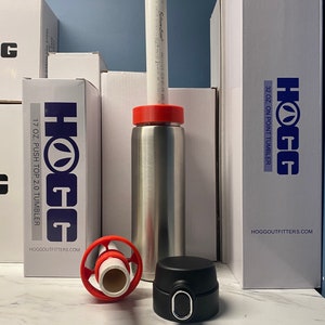 May include: A stainless steel tumbler with a red lid and a black lid, along with a white PVC pipe and several white boxes. The boxes have the "HOGG" logo and text that reads "17 OZ. PUSH TOP 2.0 TUMBLER" and "32 OZ. ON POINT TUMBLER".