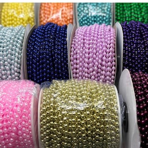 May include: A collection of multiple spools of plastic bead chains in various colors including yellow, orange, teal, green, light blue, dark blue, light pink, lavender, dark purple, gold, and bright pink, each wrapped in clear protective plastic film.