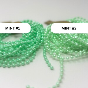 May include: Two coiled strands of mint green ball chain, labeled MINT #1 and MINT #2. Each strand consists of small, uniform, spherical beads connected by thin metal links, creating a continuous, flexible chain suitable for various functional uses.
