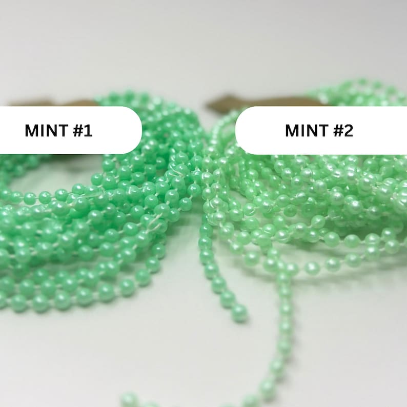 May include: Two coiled strands of mint green ball chain, labeled MINT #1 and MINT #2. Each strand consists of small, uniform, spherical beads connected by thin metal links, creating a continuous, flexible chain suitable for various functional uses.