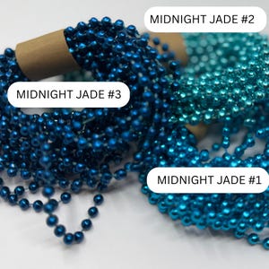 May include: Three coiled strands of metallic beads in varying shades of blue and teal. Each coil is secured with a brown paper band. The labels MIDNIGHT JADE #1, MIDNIGHT JADE #2, and MIDNIGHT JADE #3 are visible, identifying the specific color variations.