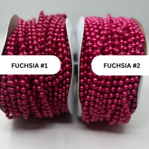 May include: Two spools of fuchsia ball chain, each featuring a continuous strand of small, round, vibrant pink beads. The left spool is labeled FUCHSIA #1 and the right spool is labeled FUCHSIA #2, both showcasing a consistent, uniform texture.